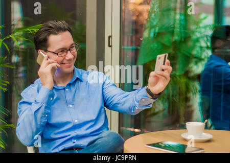Lächelnde Geschäftsmann im Gespräch mit Smartphone und geben Karte Kellner im Cafe Stockfoto