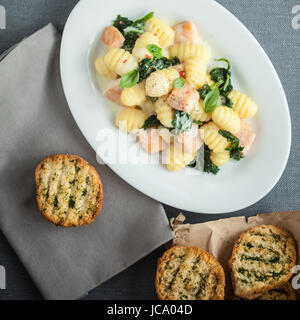 Ansicht von oben aus einer Platte italienische Gnocchi-Nudeln, Basilikum und gegrilltem Lachs Stücke mit knackig knusprig gerösteten Kräuter Brötchen serviert Stockfoto