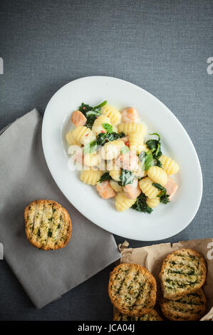 Teller mit italienischen Gnocchi Nudeln und Lachs Stücke gedünstet mit frischem Basilikum und serviert mit goldenen gerösteten Kräuter Knäckebrot, Draufsicht auf grau mit Exemplar Stockfoto