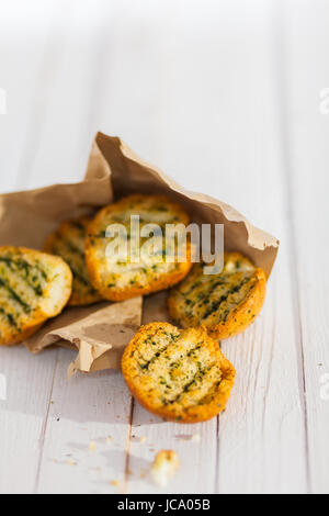 Goldenen knusprig gegrillte Kräuter Brot vom Grill aus einer zerrissenen braunen Papier-Paket auf einem rustikalen weißen hölzernen Picknicktisch mit Exemplar verschütten Stockfoto