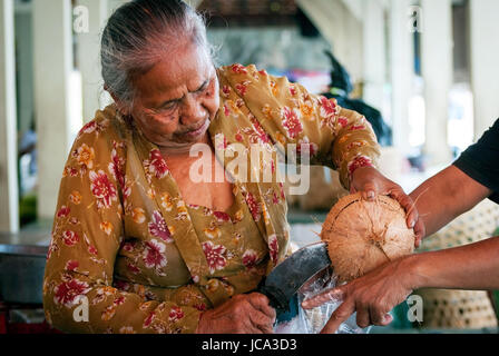 YOGYAKARTA, Indonesien - SEPTEMBER, 15: alte Frau Kokosnuss öffnen, die Kokosmilch auf dem lokalen Markt in Yogyakarta, Indonesien auf Septmber 15, 20 Stockfoto