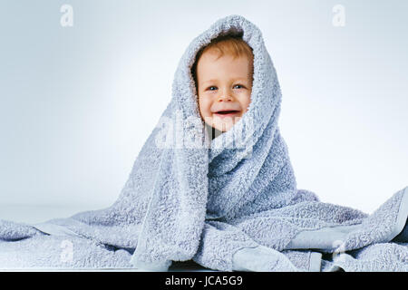 Acht Monate Baby nach dem Waschen in großen weichen Handtuch sitzen und lächelnd auf weißem Hintergrund Stockfoto