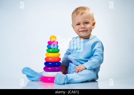 Acht Monate Baby spielt mit Spielzeug Pyramide auf weißen und blauen Hintergrund mit Reflexion Stockfoto