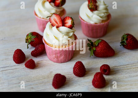 Muffins mit Sahne und süße Sahne, dekoriert mit Erdbeeren. Auf einem hölzernen Hintergrund. Stockfoto