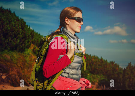 Junge Frau Tourist mit grünen Rucksack und Sonnenbrille auf Berge Hintergrund stehend Stockfoto