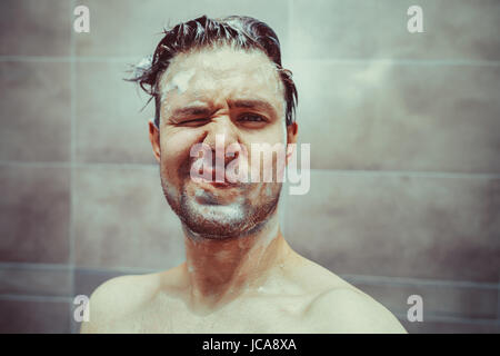 Junger Mann Waschen mit Shampoo im Bad Portrait. Unglückliche Emotionen. Stockfoto