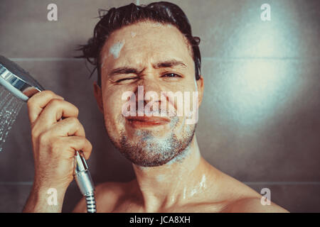 Junger Mann Waschen mit Shampoo im Bad Portrait. Unglückliche Emotionen. Stockfoto