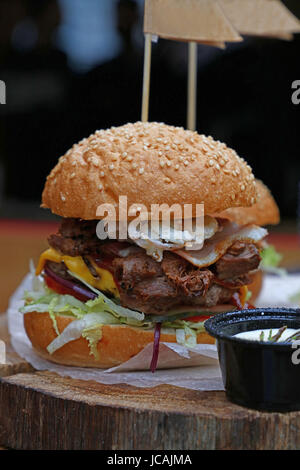 Große amerikanische Burger mit gezogenes Schweinefleisch, Zwiebelringe, Käse und Salat in Sesam Brötchen auf Pergament Papier über natürliche Holz geschnitten, Nahaufnahme, niedrigen Winkel Stockfoto