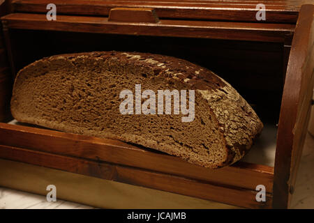 Die Hälfte der Artisan schwarz frisches Schwarzbrot Laib in traditionellen rustikalen Vintage Holz Breadbin Feld, Nahaufnahme, niedrigen Winkel Ansicht Stockfoto