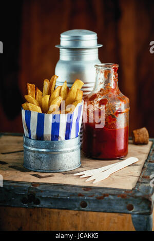 Bunte blau gestreiften Packung von Pommes frites, stehend auf einem rustikalen Holztisch im Ladengeschäft Fish and Chips mit Gewürzen knusprig Stockfoto