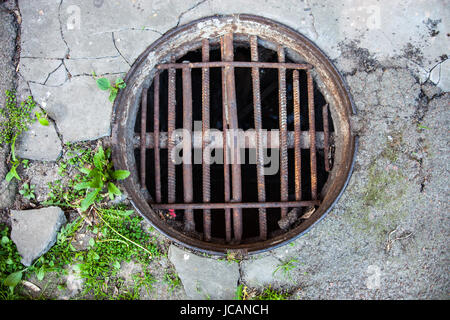 Manhole with the handmade metal armature cover in the cracked concrete and asphalt surface Stockfoto