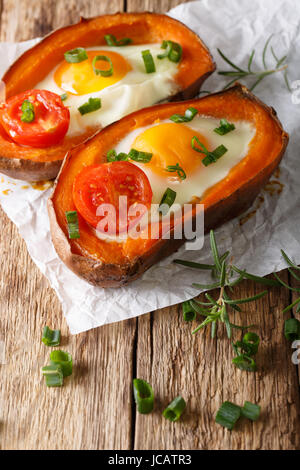 Lecker gebackene Süßkartoffel gefüllt mit gebratenem Ei und Tomate Nahaufnahme auf dem Tisch. Vertikal Stockfoto