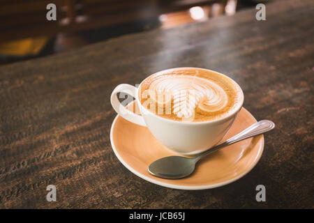 Enge Fokussierung auf heißen Cappuccino Tasse mit Latte Art on dunkel braun Holztisch. Stockfoto