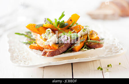 Gourmet Kürbis-Salat mit gebratenem Hokkaido und gegrilltem Brot. Auf weißer Holztisch serviert. Stockfoto