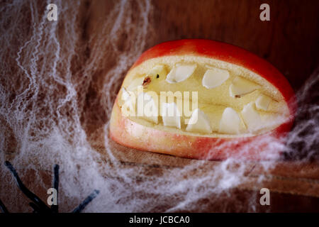 Gruseligen klaffende Halloween Mund mit Zähnen gemacht aus einem Apfel auf einem Holzregal behängt mit Spinnweben in einem beängstigend festlichen Hintergrund für Allhallows Eve Stockfoto