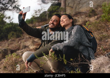Junges Paar in Liebe auf Bergweg und nehmen Selfie sitzen. Glücklicher junger Mann und Frau in Landschaft wandern und Selbstbildnis mit Mobil im Gespräch Stockfoto