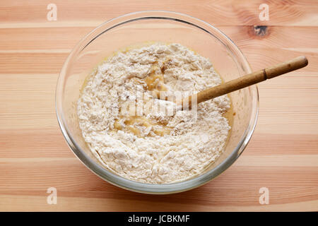 Mehl wird in feuchten Teig für Bananen Brot in eine Glasschüssel auf einem Holztisch gerührt Stockfoto