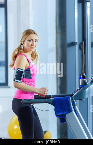 Schöne blonde Frau in Sportbekleidung training auf Laufband und lächelt in die Kamera Stockfoto