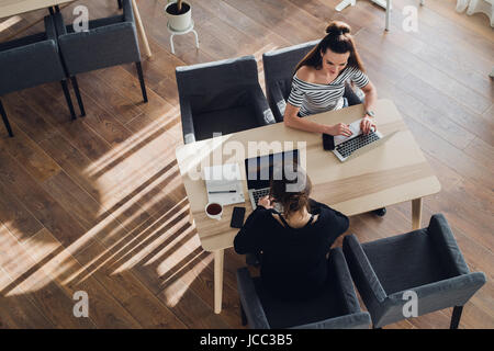 Draufsicht der junge Frau trägt eine Smartwatch auf ihrem Laptop in einem Café arbeiten. Ansicht von oben geschossen weiblichen sitzen an einem Tisch mit einem Telefon in der Nähe und Surfen Internet. Stockfoto
