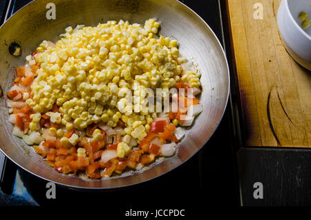 Mais-Paprika und Zwiebeln in der Pfanne anbraten auf dem Herd Stockfoto