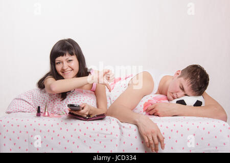 Junges Mädchen und ein Mann im Bett. Schönes Mädchen hat gepflegte Nägel auf der Hand, der Kerl gerade Fußball im Fernsehen Stockfoto