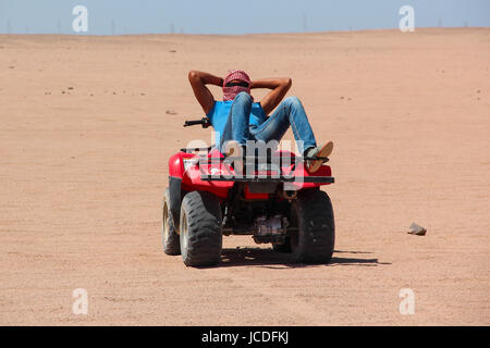 HURGHADA, Ägypten - 24. April 2015: Ein junger ägyptischer Mann ruht auf seinem ATV nach Wüstensafari auf Quad, Ägypten, HURGHADA am 24. April 2015 liegen. Stockfoto