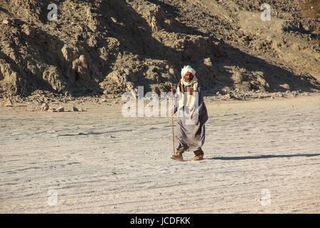 HURGHADA, Ägypten - 24. April 2015: Die alten Beduinen mit einem Stock zu Fuß durch die Wüste auf dem Hintergrund Sand und Berge Stockfoto