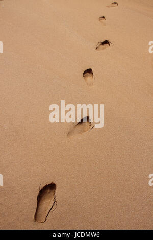 Sechs tiefen Spuren März diagonal in eine Linie über den Sand am Strand; Beachcomber oder verlorene Seele, einfachen Bild zu Fuß aus dem Rahmen. Stockfoto