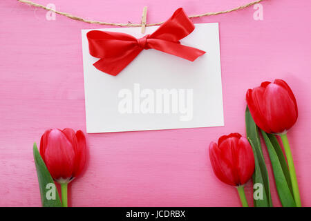 Textkarte mit Wäscheklammern über rote Tulpen und rosa Holzbrett hängen Stockfoto