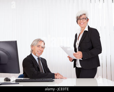 Ein senior Manager sitzt an seinem Schreibtisch und seine Sekretärin oder Assistentin Stockfoto