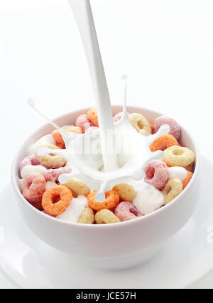 Gießen frischen cremigen Milch in eine Schüssel mit bunten Obst Müsli in eine weiße Keramikschale mit einem Schuss auf einen weißen Hintergrund mit Exemplar Schleifen Stockfoto