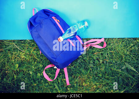 Sommer sportlichen Hintergrund. Eine Flasche Wasser und Rucksack auf Gymnastikmatte von oben auf den grünen Rasen Hintergrund. Stockfoto