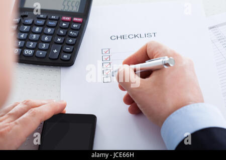 Nahaufnahme von Hand mit Stift über Antragsformular mit Handy und Rechner Stockfoto