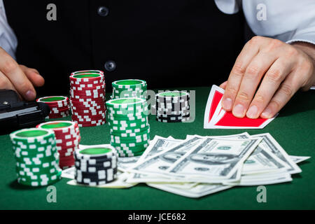 Porträt von einem Croupier Spielkarten mit Pistole und Stapel von token Chips am Tisch zu betrachten Stockfoto