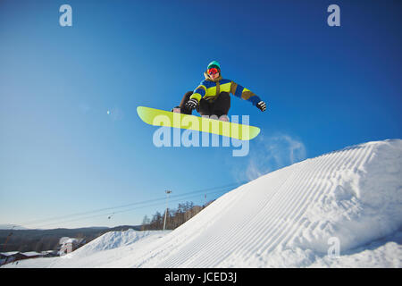 Porträt des jungen Mannes, Snowboarden im Winter gegen blauen Himmel Stockfoto