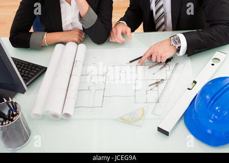 Draufsicht eines männlichen und weiblichen Architekten diskutieren eine Reihe von Plänen, die auf einem Tisch ausgebreitet beschnitten Stockfoto