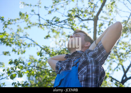 Closeup Portrait des mittleren Alter Mann in Arbeitskleidung mit gekreuzten Händen auf Kopf Stockfoto