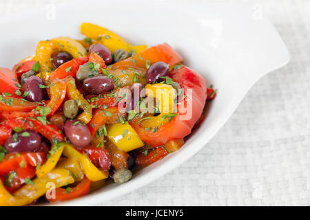 Paprika gekocht in Pfanne mit Öl, Oliven und Kapern. Typisch italienische Küche, zum Verzehr bereit. Weiße Schale auf weißem Hintergrund. Stockfoto