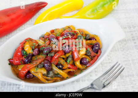 Paprika gekocht in Pfanne mit Öl, Oliven und Kapern. Typisch italienische Küche, zum Verzehr bereit. Weiße Schale auf weißem Hintergrund. Stockfoto