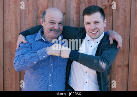 Vater und Sohn auf hölzernen Hintergrund. Sie blicken auf Kamera und Lächeln zufrieden. Stockfoto