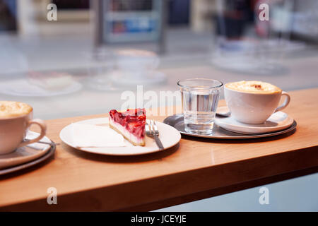 Ein Stück Erdbeer Käsekuchen, Glas Wasser, Andcupsof Kaffee im Frontof-Fenster in einem Café. Stockfoto