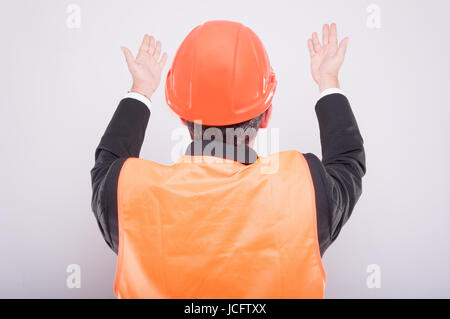 Rückansicht des Ingenieurs zu zeigen oder erklären, etwas mit Bauarbeiterhelm und reflektierende Weste auf grauem Hintergrund Stockfoto