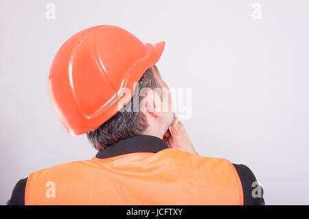 Rückansicht des Ingenieurs denken Geste mit Bauarbeiterhelm und reflektierende Weste auf grauem Hintergrund Stockfoto