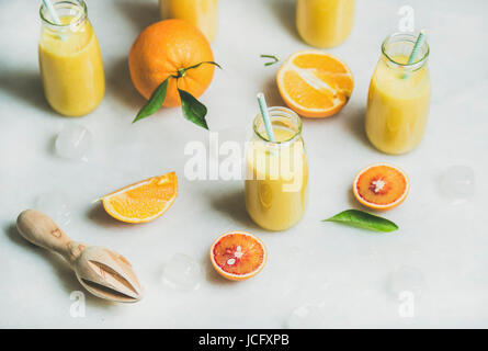 Gesunde gelbe Smoothie mit Zitrusfrüchten, Ingwer, Eis in Glasflaschen über leichte Marmortisch Hintergrund, selektiven Fokus. Sauberkeit, Essen, Vegan, Gemüse Stockfoto