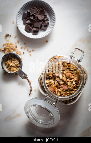 Erdnussbutter-Müsli mit Kakaonibs und gehackten Mandeln und dunkler Schokolade mit Milch auf einen Marmortisch in Draufsicht Stockfoto