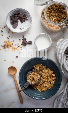 Erdnussbutter-Müsli mit Kakaonibs und gehackten Mandeln und dunkler Schokolade mit Milch auf einen Marmortisch in Draufsicht Stockfoto