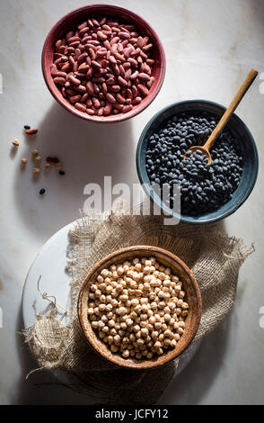 Garbanzo Bohnen/Kichererbsen, Bohnen/Rajma, schwarze Bohnen in einzelnen Keramikschalen auf einen Marmortisch in Draufsicht Stockfoto