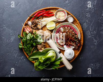 Zutaten für die asiatische Küche mit Tiger Garnelen, Udon-Nudeln, Champignons, grünen Gemüse, Kochen Gewürze auf Bambus Tablett auf dunklem Hintergrund Stockfoto