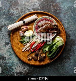 Zutaten für asiatische Kochen mit Tiger Garnelen, Udon-Nudeln, Champignons, grünen Gemüse, Gewürze auf Bambus Tablett auf Metall Hintergrund Stockfoto