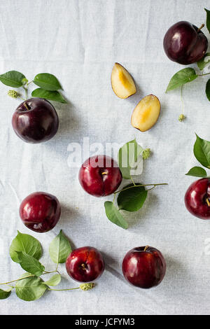 Pflaumen mit Blättern über weißen Tisch Stockfoto